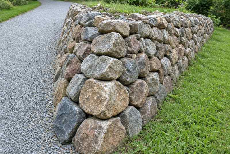 Natural fieldstone retaining wall alongside a gravel path.