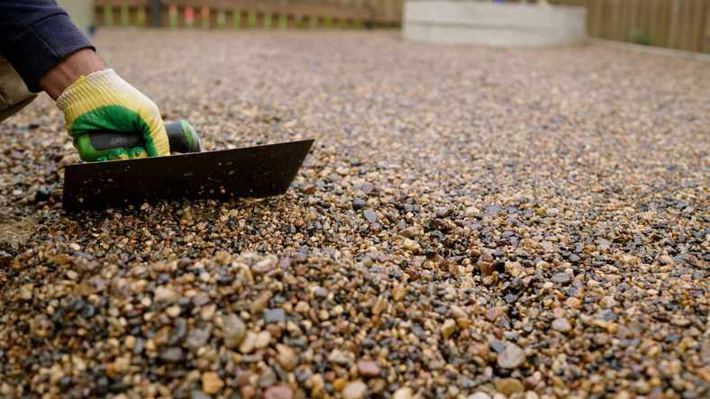 Landscaper spreading decorative landscaping gravel, leveling surface with a trowel.