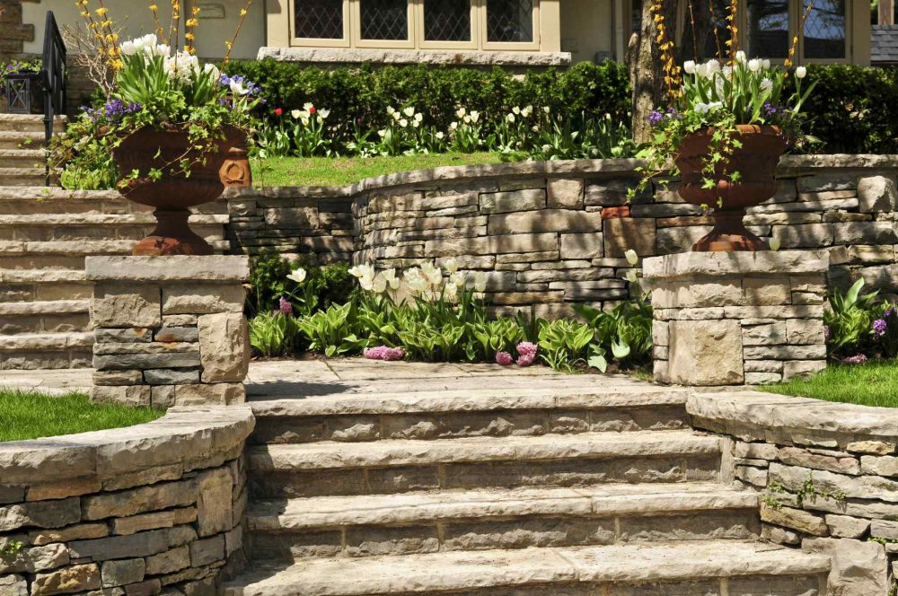Natural stone steps, posts, landscaping and retaining wall in front of a house