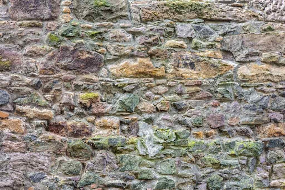 Old weathered stone wall using rough fieldstone with moss or lichen growth