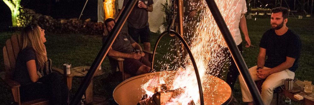 A firepit grill lit at night with friends seated around it