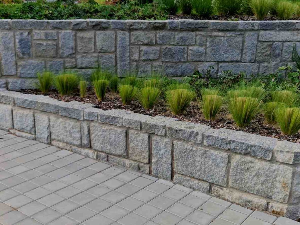 Granite retaining wall stones against a stone path with small green plants.