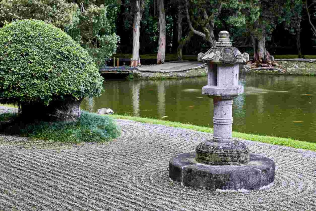 Zen garden with large pond in the background, sand in foreground, neatly trimmed bushes.