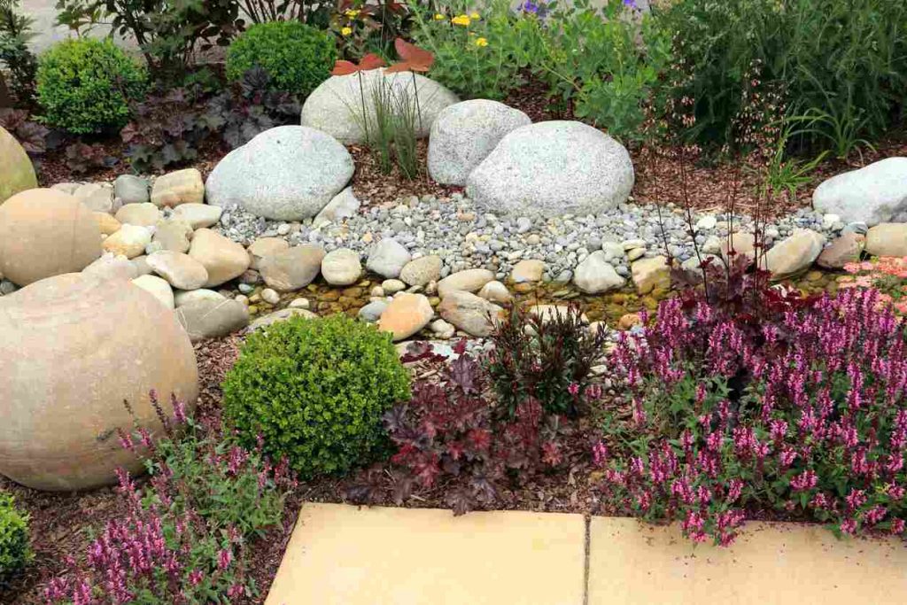 River rock landscaping utilizing multiple sizes of natural stone and a water feature, surrounded by beautiful natural greenery.