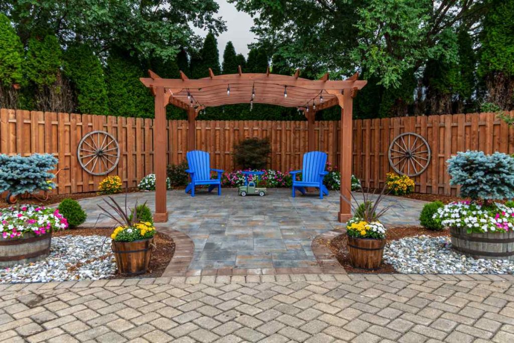 Wooden pergola on pavers patio design with colorful ornamental flowers and evergreens in a Columbia, MO backyard oasis!