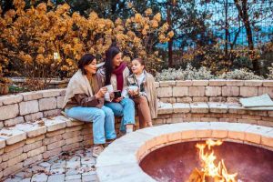 Elderly mother, adult daughter and dranddaughter sitting by fire pit at evening.