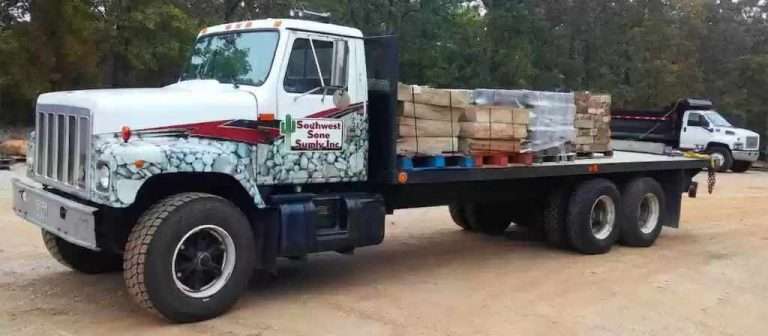 A white Southwest Stone Supply flatbed truck loaded with pallets of landscaping stone delivered to Columbia MO backyard landscaping project.