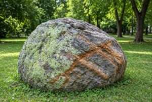 A large natural stone boulder with lichen in a garden.