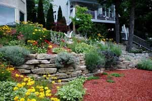 A stone ledge rock raised flower bed with red cedar mulch and flowers