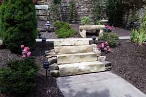 Stone steps surrounded by mulch, with a stone bench in the background
