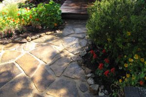Attractive flagstone pavers in a walkway with shrubs alongside.